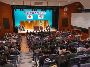 二十歳のつどいへの参加者が文化ホールに着席している様子。壇上には市長、教育長、来賓の2人が着席している。