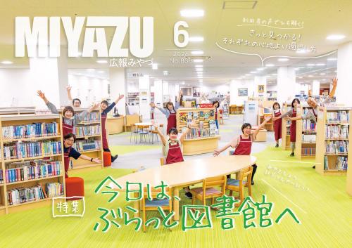 本棚の近くで図書館の10数名職員が笑顔で両手を広げている様子