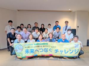 イベントへの参加者20人が横断幕の後ろに並んで立って笑顔を見せている様子