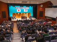 二十歳のつどいへの参加者が文化ホールに着席している様子。壇上には市長、教育長、来賓の２人が着席している。